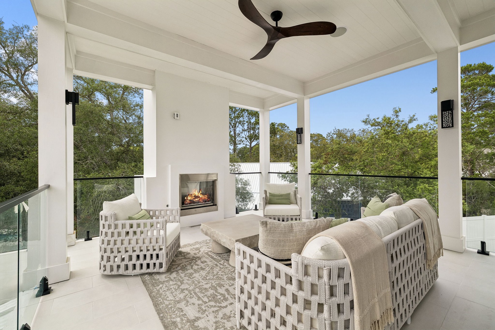 Unwind in your private covered terrace, where elegant seating circles a cozy fireplace beneath a modern ceiling fan. Surrounded by lush treetop views, this serene outdoor living space invites relaxation any time of day.