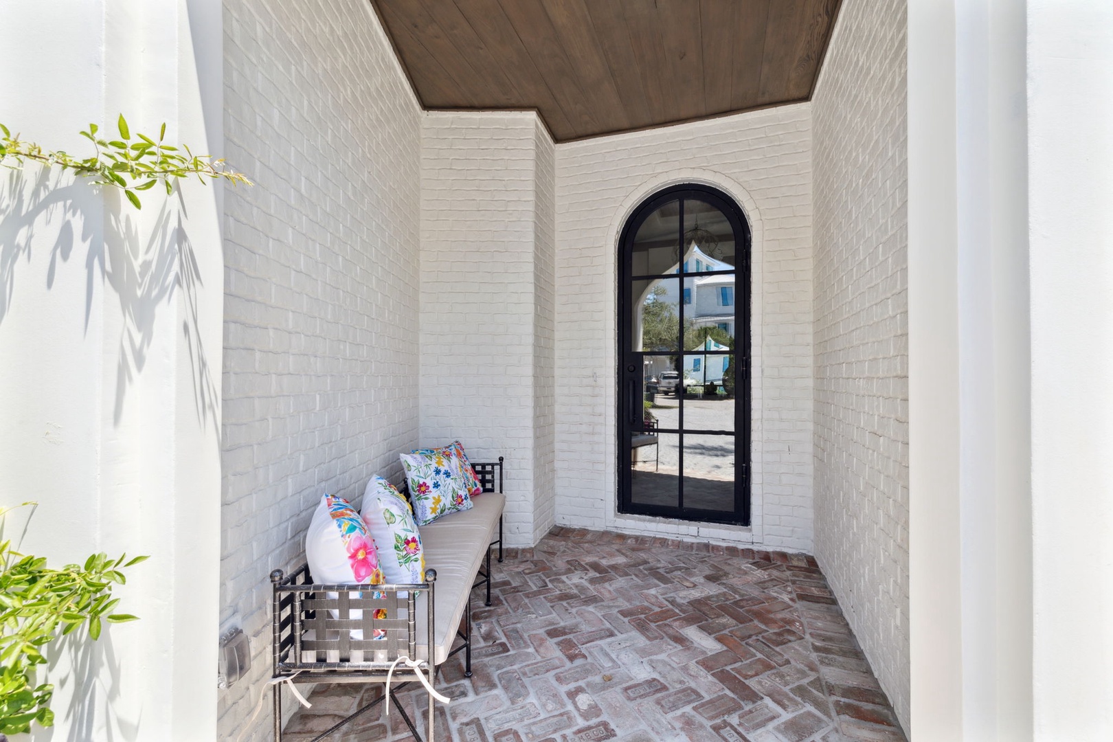 A welcoming front entrance features textured white brick walls, warm wooden ceiling details, and herringbone brick flooring. A cozy bench invites you to pause and take in the charming arrival experience.