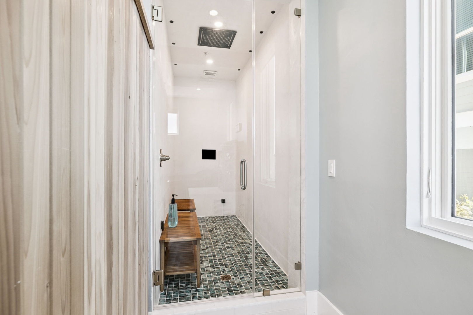 Step into your spa-like shower sanctuary with rainfall head, mosaic tile floors, and teak bench for ultimate relaxation.