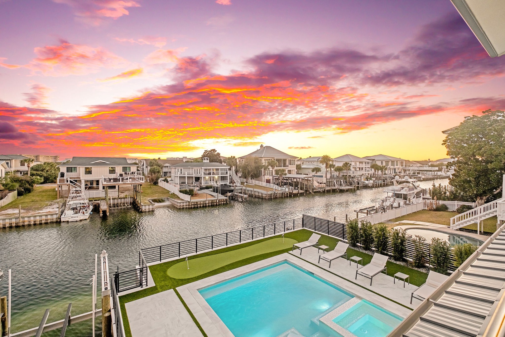 Stunning waterfront property featuring a pristine pool area overlooking peaceful canal waters, surrounded by luxury homes beneath dramatic sunset skies.