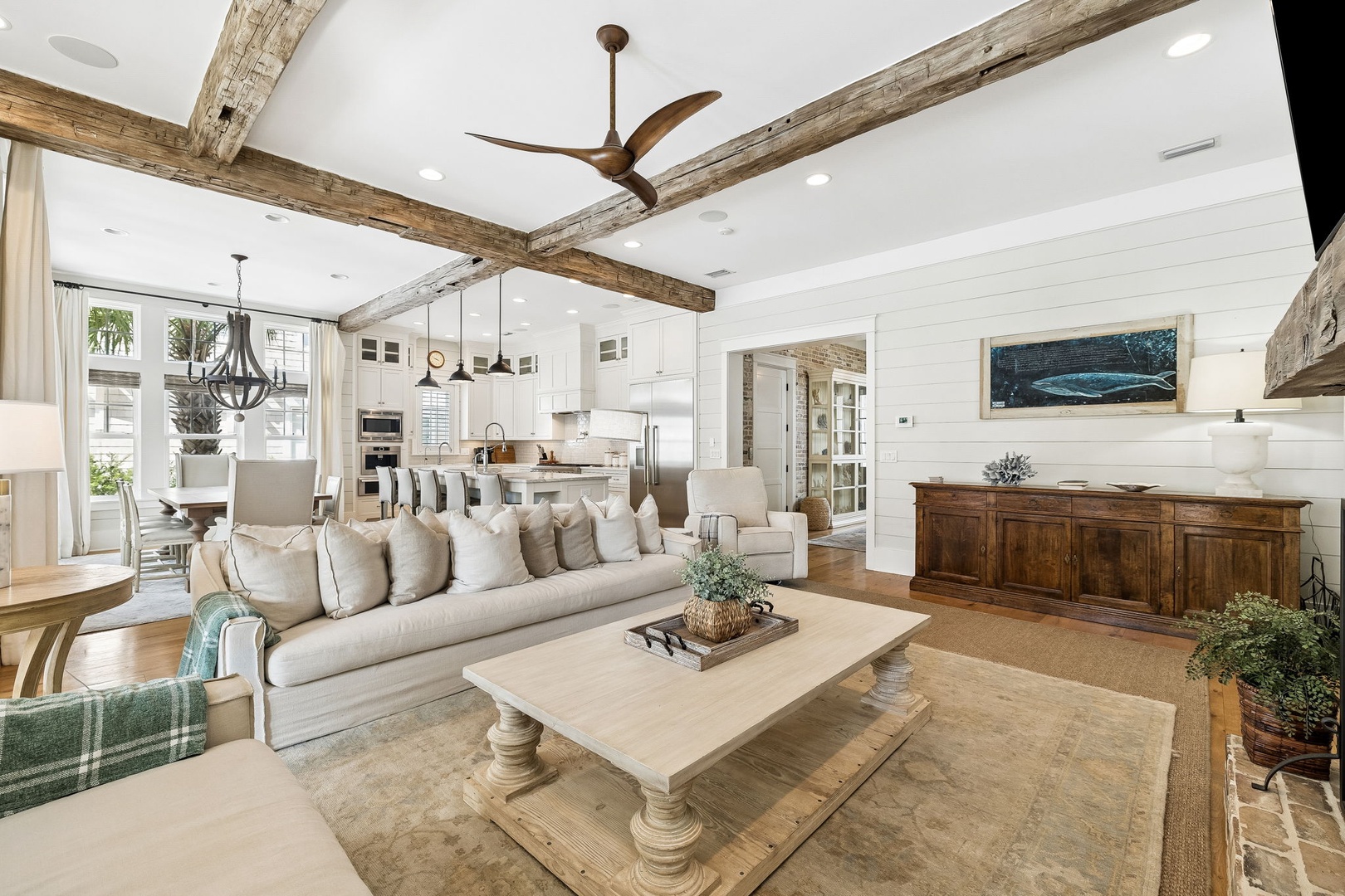 Relax in your open-concept living room, where rustic beamed ceilings meet bright coastal elegance. Sink into plush seating while enjoying breezes from the nearby windows and seamless flow to the gourmet kitchen.