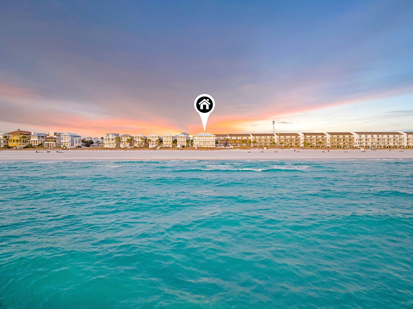 Beachfront property location showcasing crystal-clear turquoise waters, pristine sandy shore, and coastal architecture beneath a stunning pastel sunset sky.