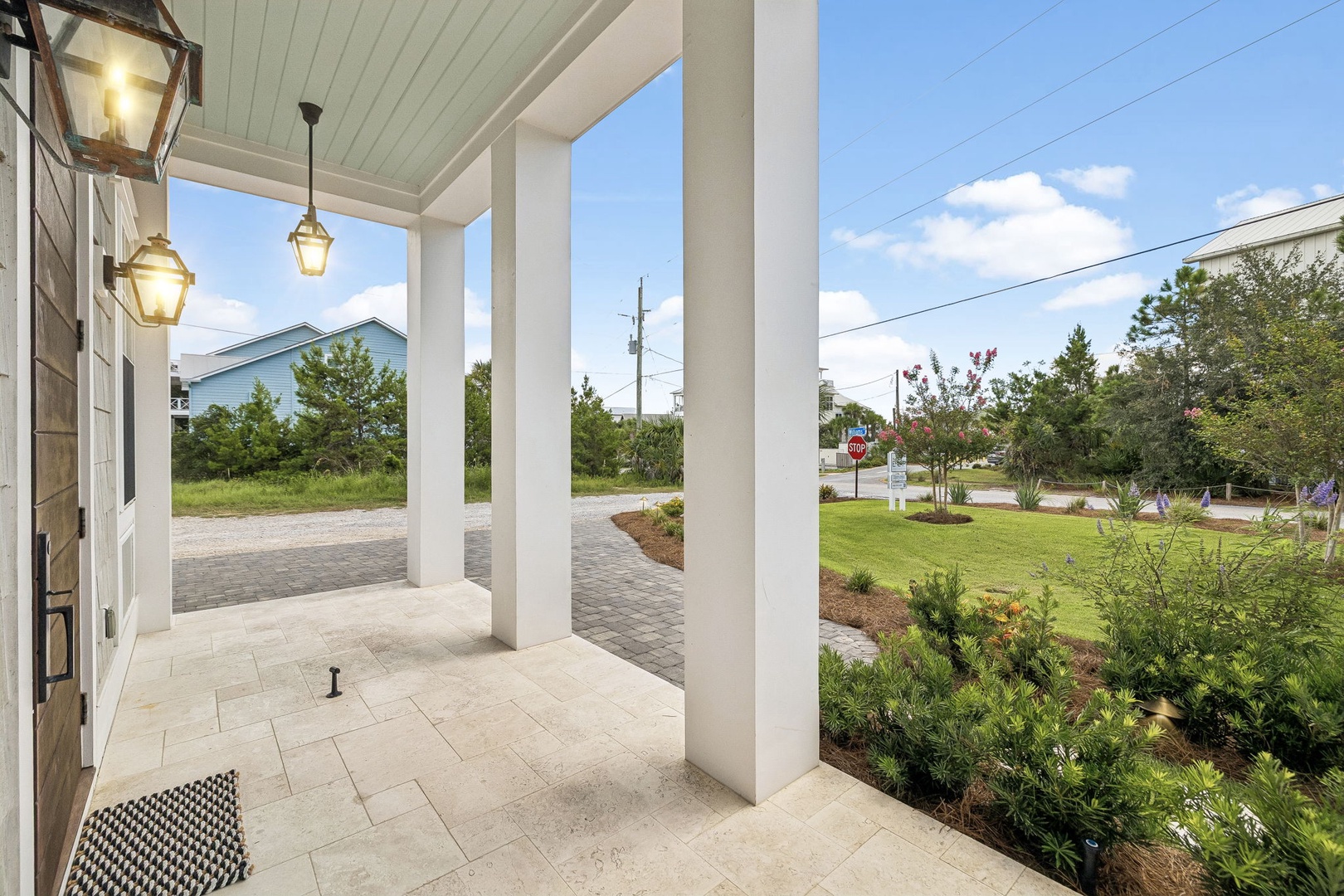A welcoming covered porch with elegant lighting frames the property's peaceful residential setting, surrounded by landscaped greenery and convenient paved parking.