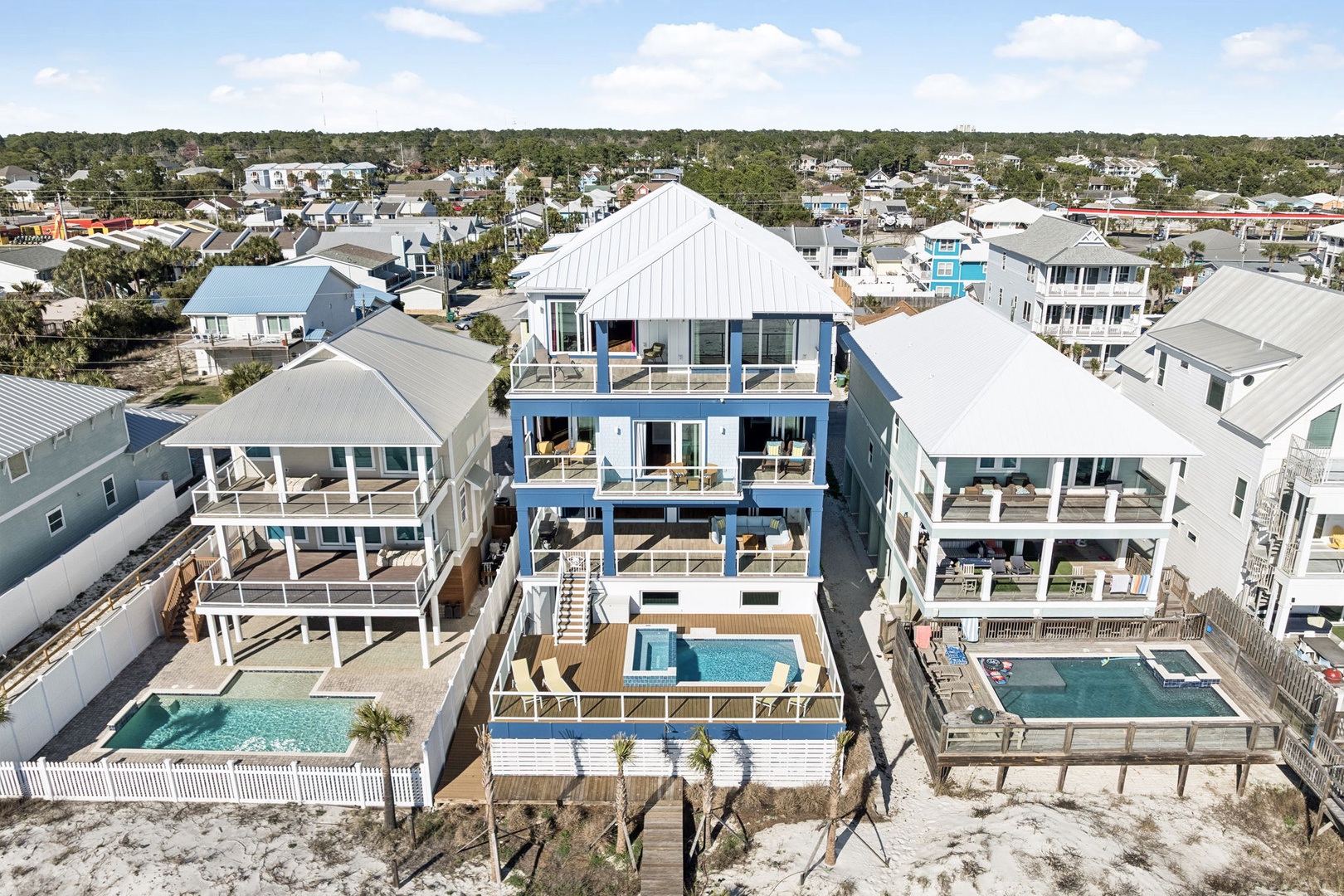 Aerial view of coastal vacation rental homes featuring swimming pools and elevated architecture in a beach community setting.