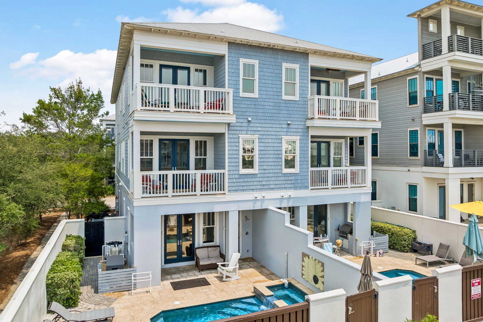 A three-story coastal retreat featuring twin private pools, spacious balconies on every level, and lush green surroundings. The property offers a serene outdoor setting with dedicated lounging areas.