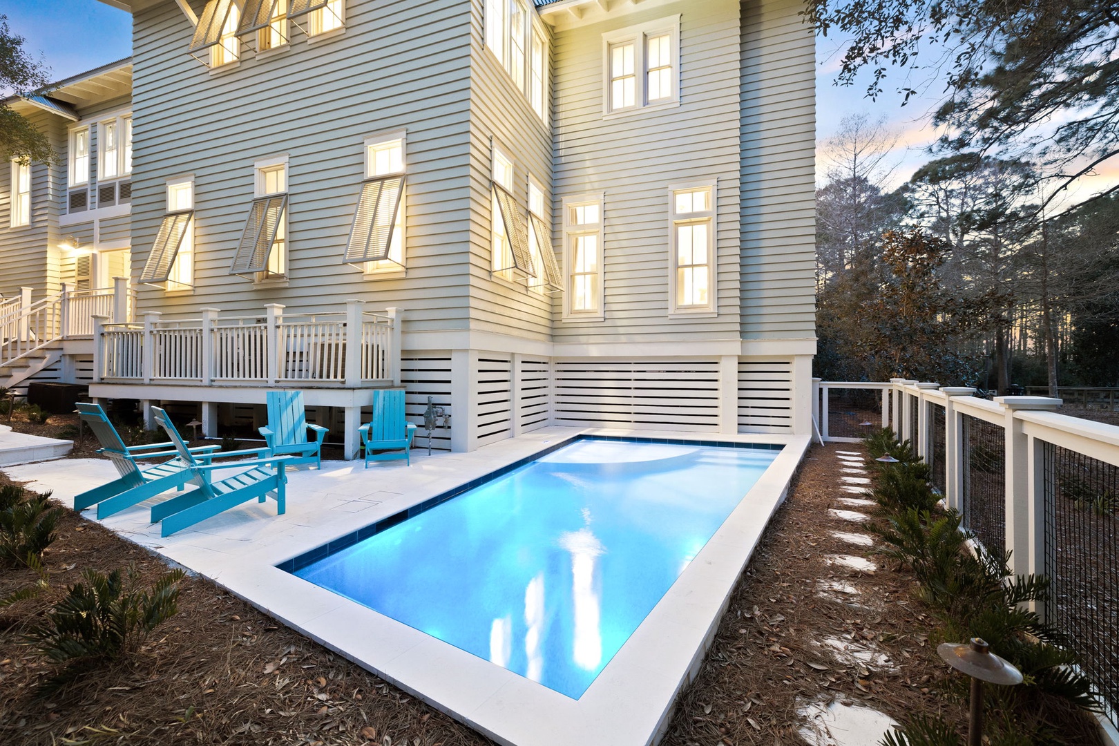 Modern coastal retreat with private swimming pool glowing at twilight, surrounded by elegant architecture and natural landscaping.