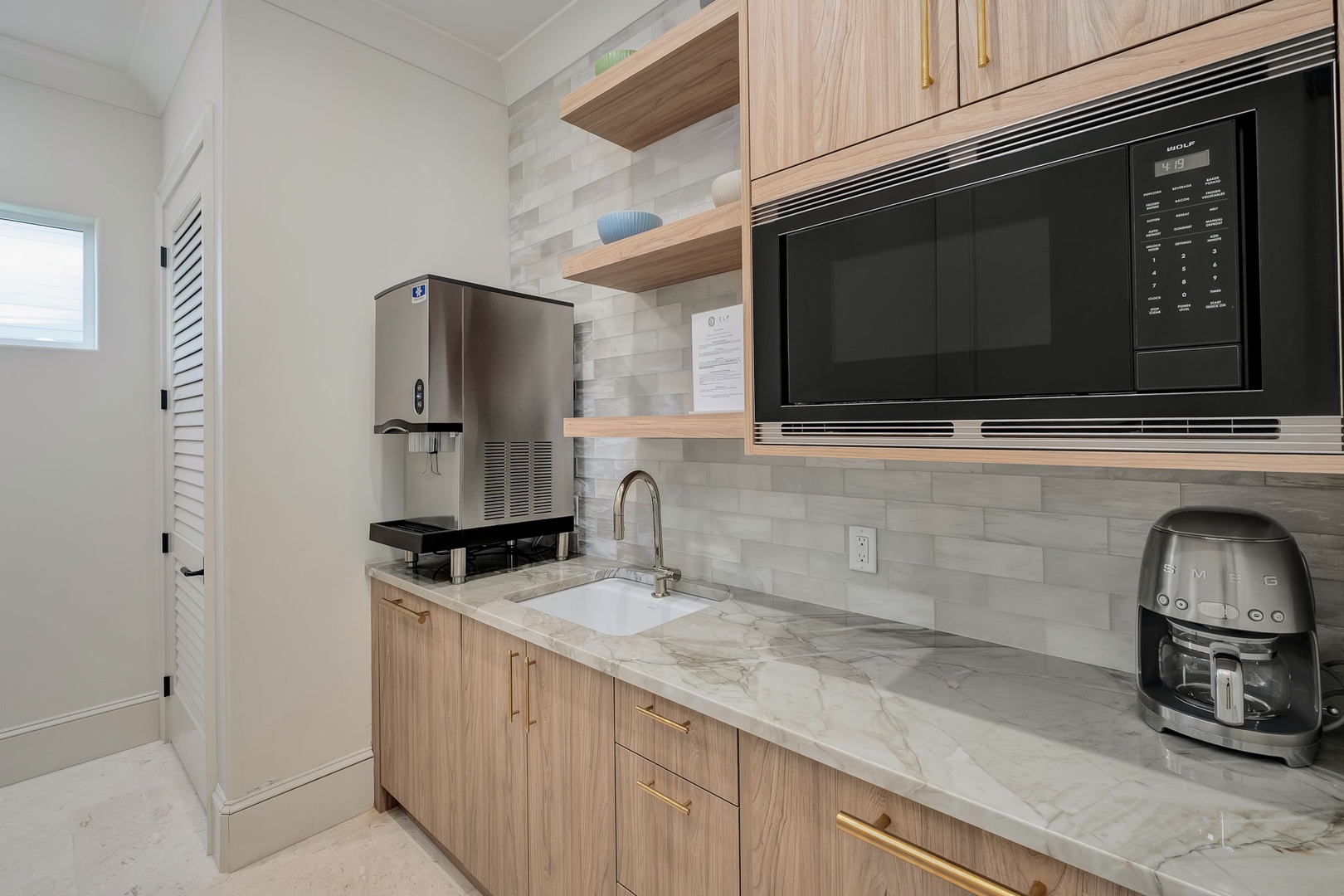 Prepare your morning coffee in this modern kitchenette featuring marble countertops, stylish light wood cabinetry, and convenient appliances including a built-in microwave and ice maker for your stay.