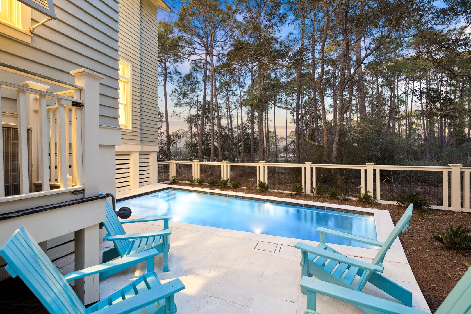 Unwind in your private poolside paradise with turquoise Adirondack chairs and forest views as twilight paints the sky.