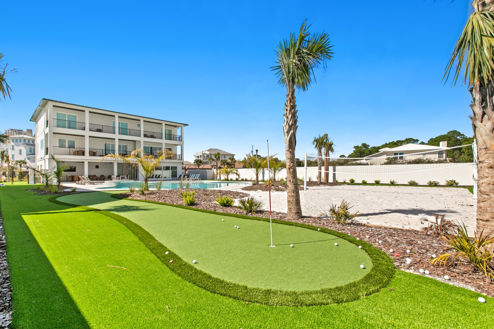Pristine putting green nestled under swaying palms and clear blue skies, with modern accommodations and a sparkling pool just steps away for the perfect coastal getaway.