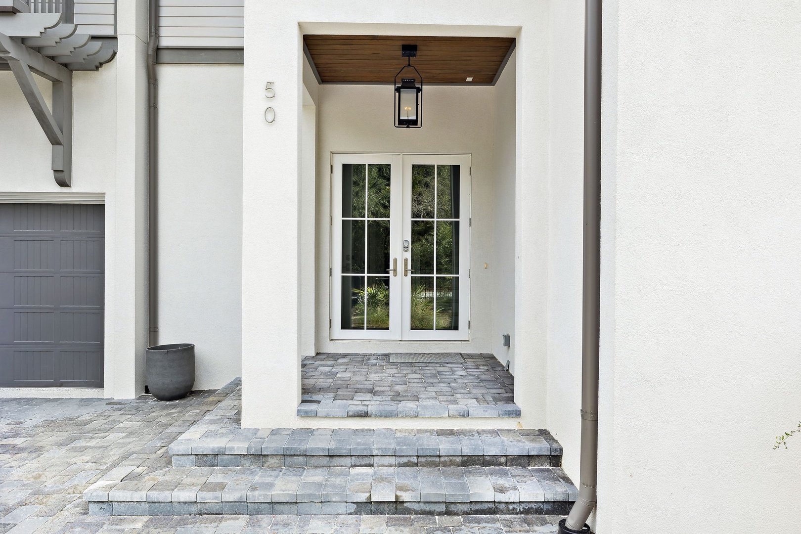 Elegant stone steps lead to the modern main entrance with French doors and warm wood ceiling details.