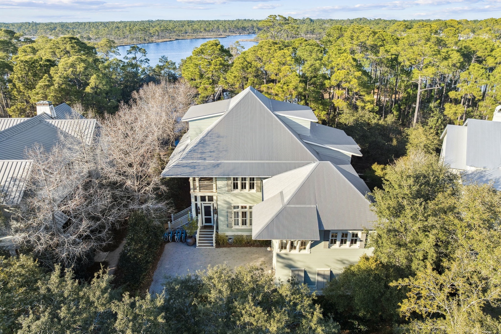 Aerial view of this stunning coastal property nestled among lush trees with water views in the distance.
