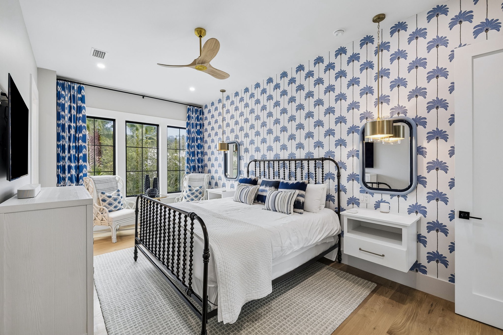 Your coastal-inspired bedroom features crisp white linens and calming blue palm wallpaper, with natural light streaming through windows overlooking greenery.