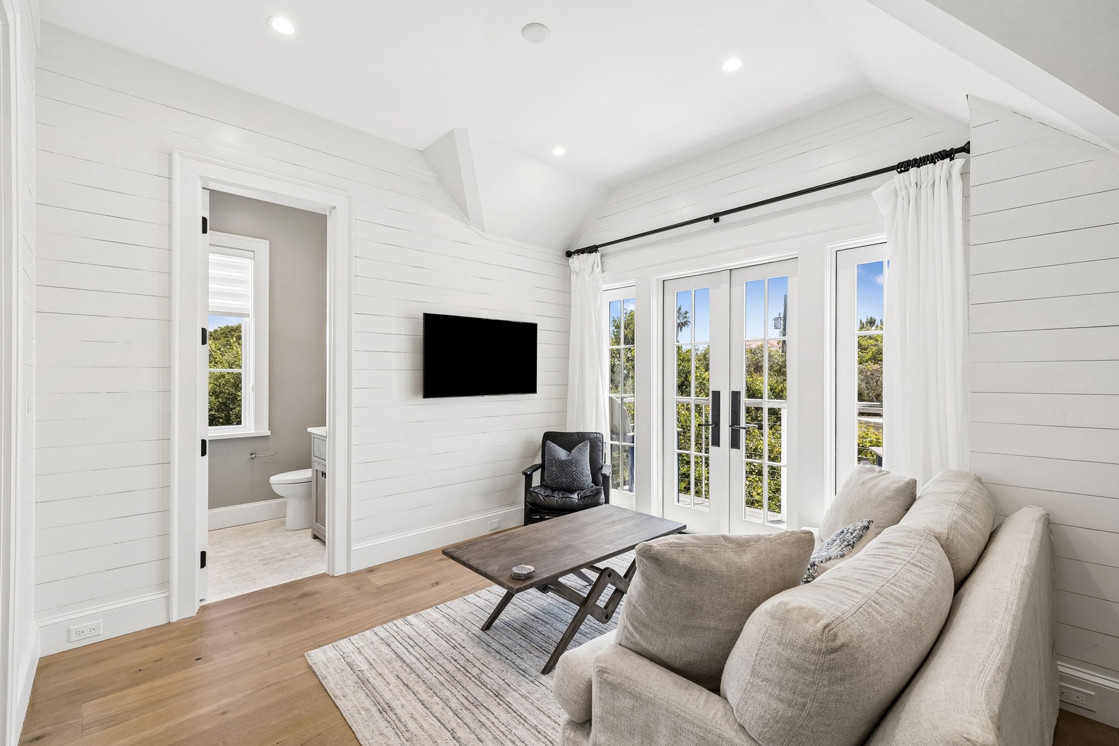 Your serene retreat features shiplap walls, vaulted ceilings, and French doors opening to greenery. Sink into the cozy sofa, catch up on your favorite shows, and let natural light fill your space.