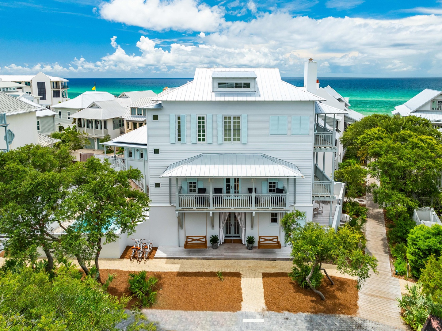 Stunning coastal home with pristine white facade and welcoming entrance, nestled among lush greenery just steps from turquoise waters.