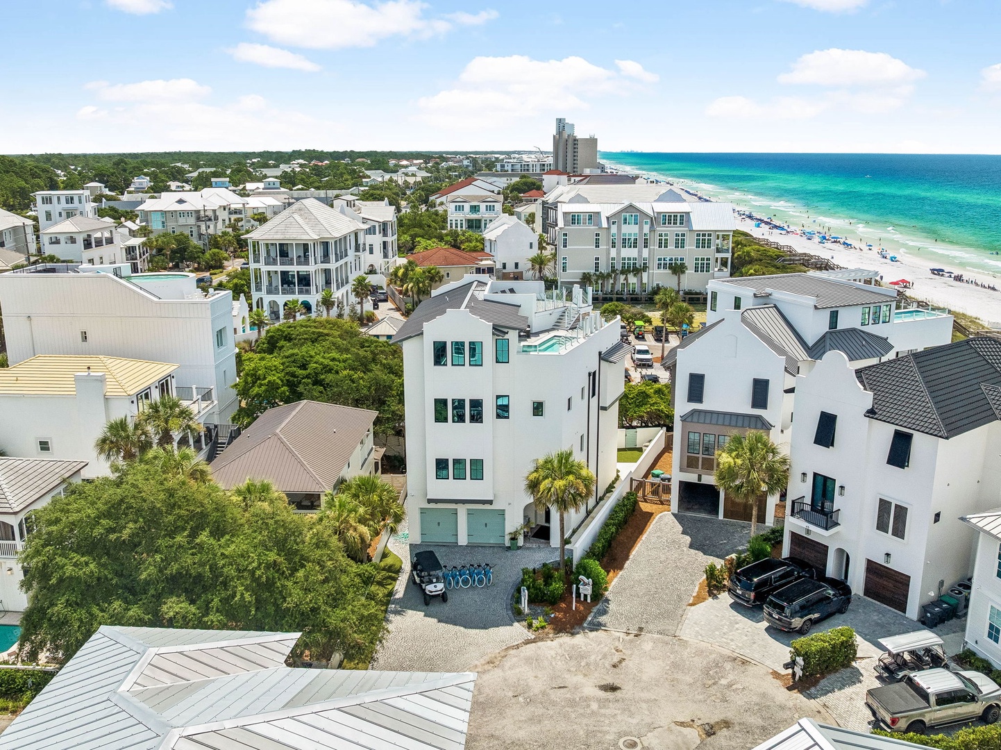 Aerial view of a coastal neighborhood featuring residential properties nestled among palm trees and lush vegetation, with pristine turquoise waters and white sandy beaches just beyond.
