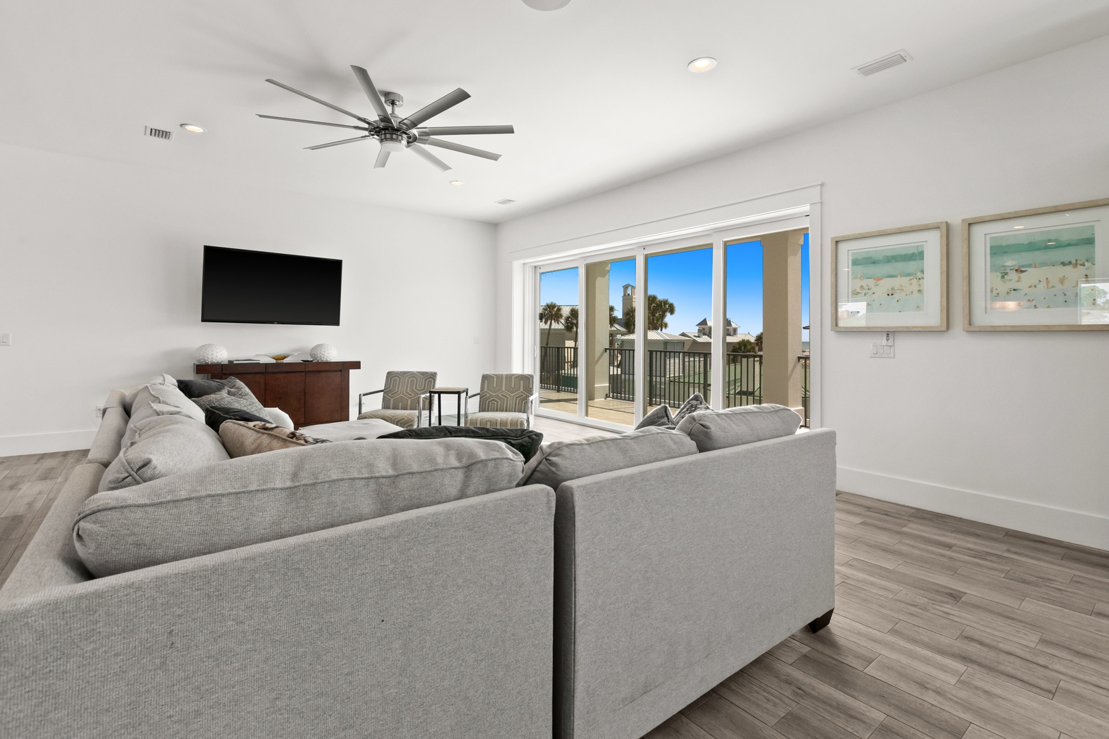 Unwind in this bright, spacious living room where coastal breezes and palm-lined views flow through expansive glass doors, inviting you to relax on plush seating after a day of adventures.