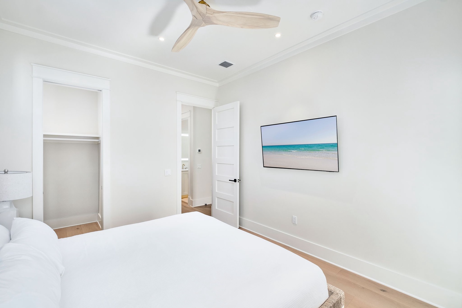 Your bedroom is a serene haven with crisp white linens, gentle overhead fan, and soft natural light streaming in. A private ensuite and ample closet space complete this peaceful retreat.
