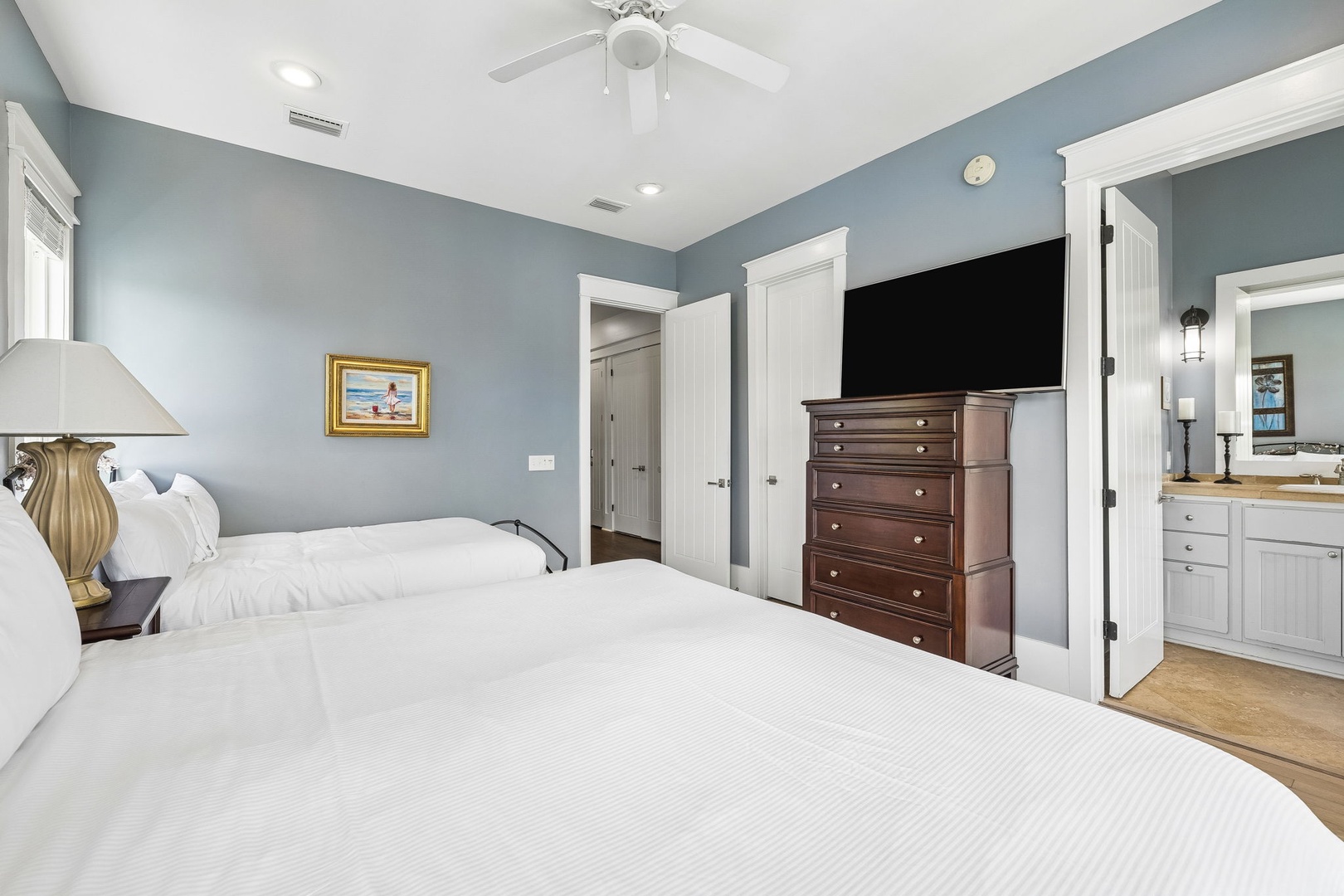 Drift off in this serene coastal bedroom, where calming blue-gray tones and plush white linens create your perfect retreat. A ceiling fan keeps you cool, while the TV and ensuite bath add comfort for effortless relaxation.