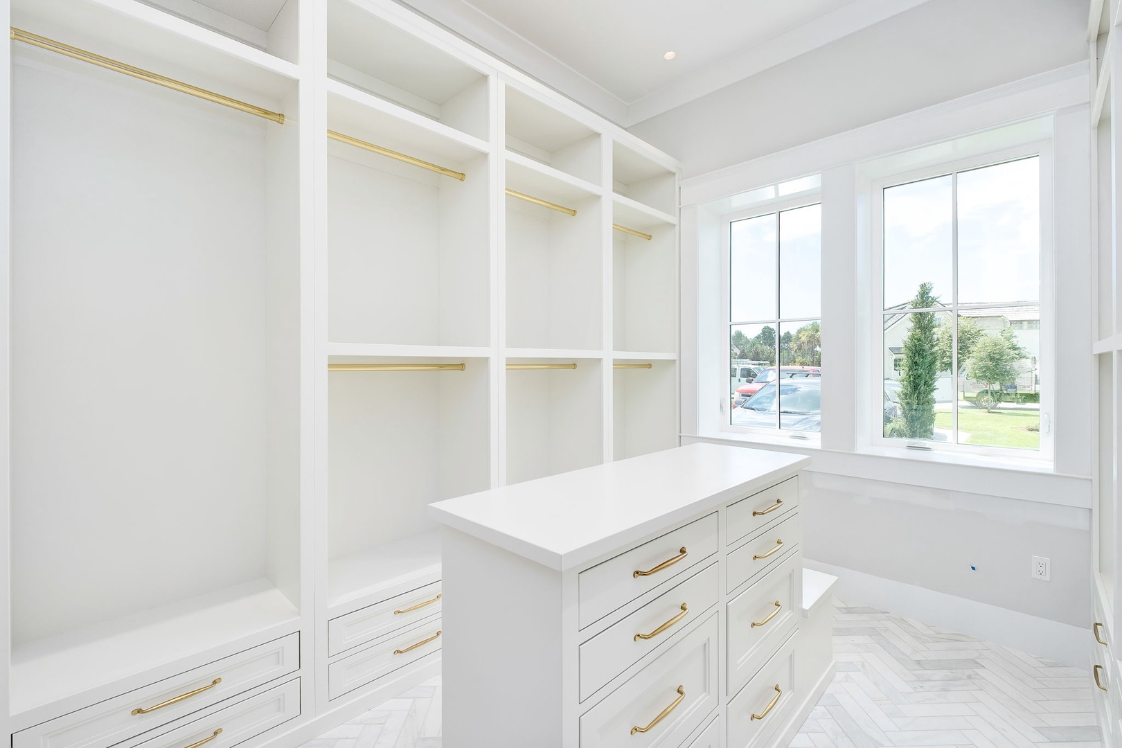 Spacious custom closet with elegant brass-accented storage awaits to hold your wardrobe in style. Large windows flood the space with natural light, making getting ready each day a delight.