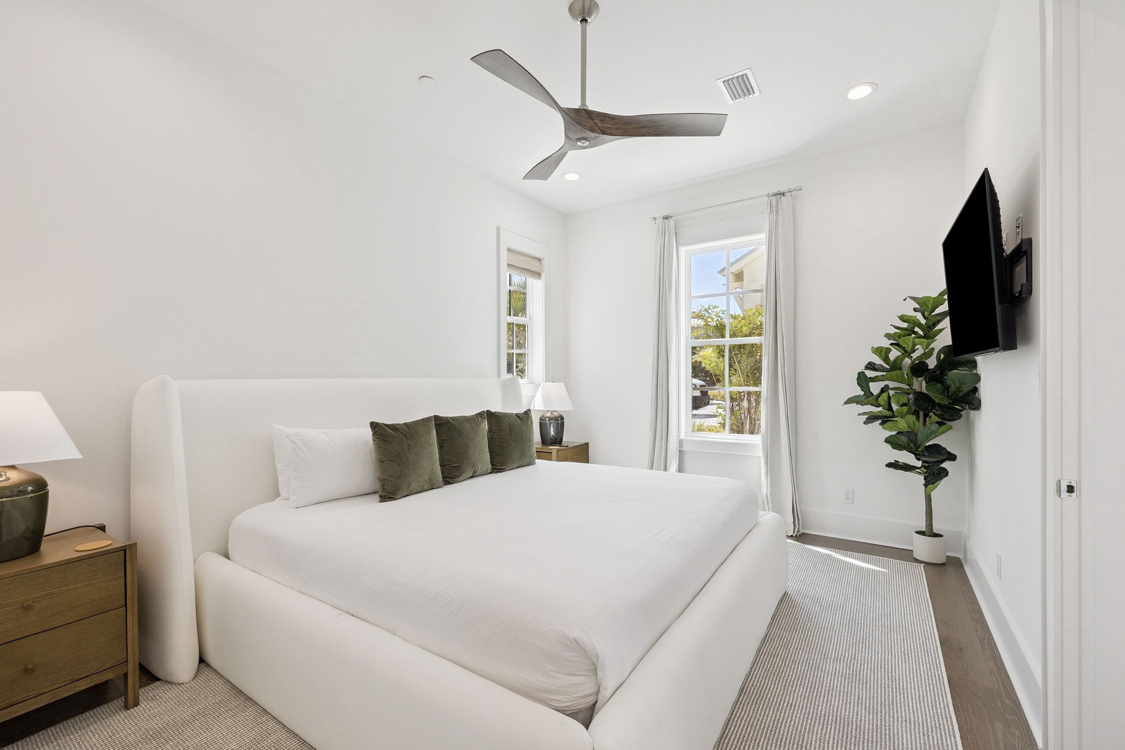 Sink into crisp white linens while the ceiling fan keeps you cool in this bright, serene bedroom with natural light streaming through.