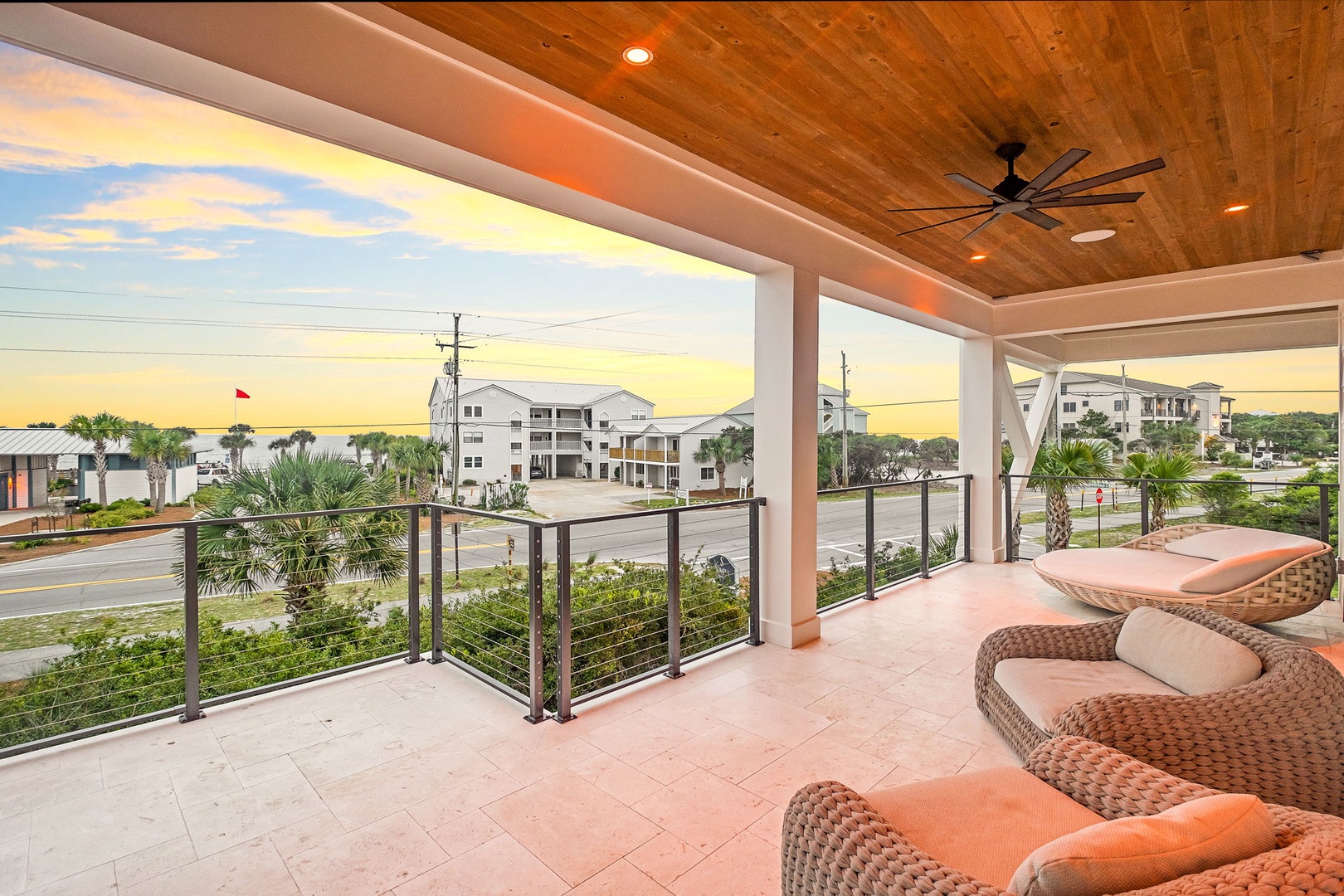 Covered terrace overlooking the neighborhood at sunset, featuring comfortable wicker seating, modern ceiling fan, and warm wood ceiling—a peaceful spot to unwind at the end of the day.