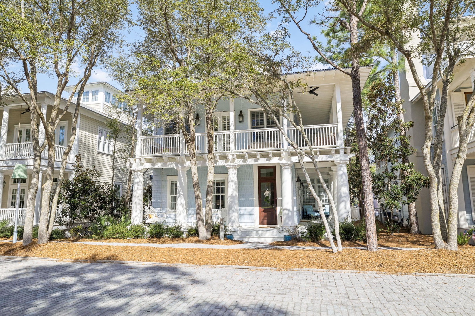 Charming coastal-style home with covered porches and natural landscaping in a peaceful tree-lined neighborhood setting.