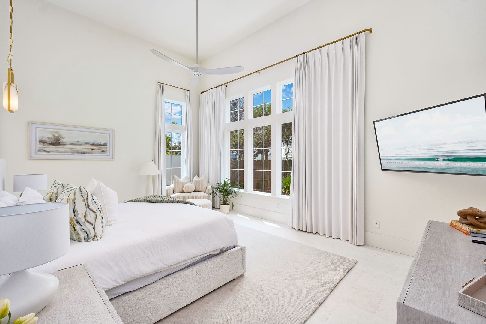 Step into your serene retreat where natural light streams through elegant floor-to-ceiling windows, casting a peaceful glow across plush white linens and calming coastal artwork that invites restful dreams.