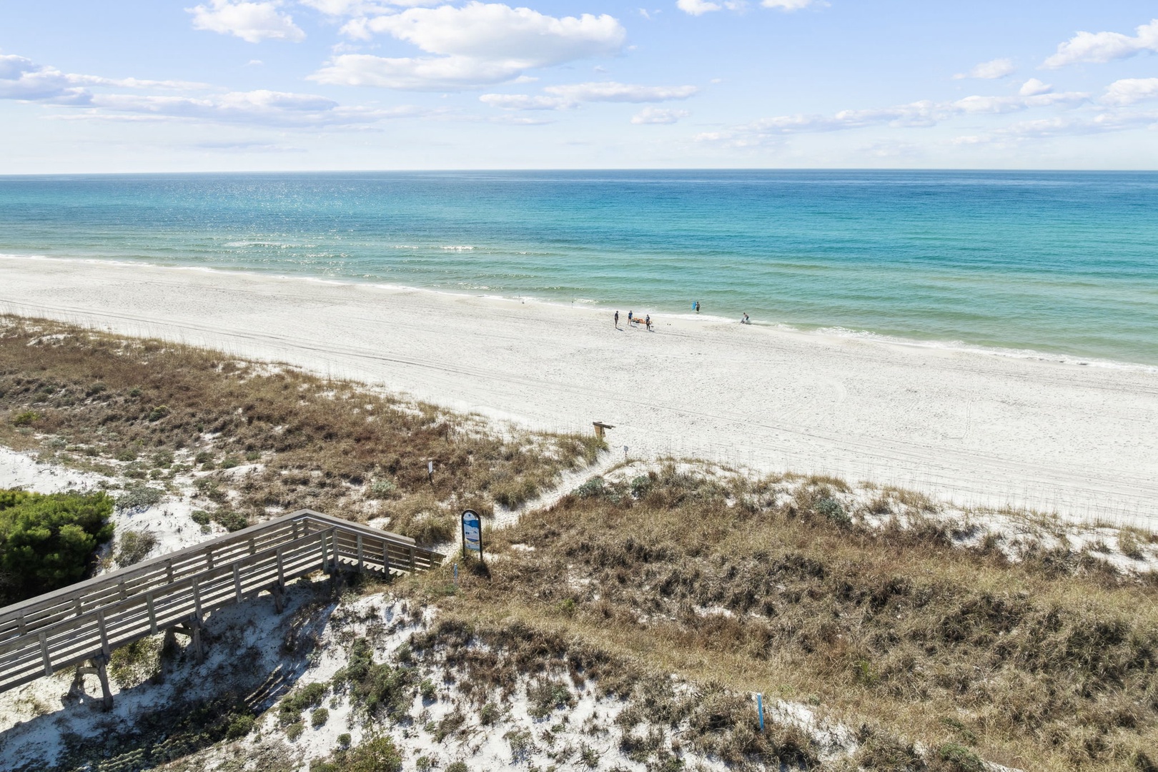 Pristine white sand beach with turquoise Gulf waters, accessed by a scenic walkway through natural coastal dunes with beachgoers enjoying the shoreline.