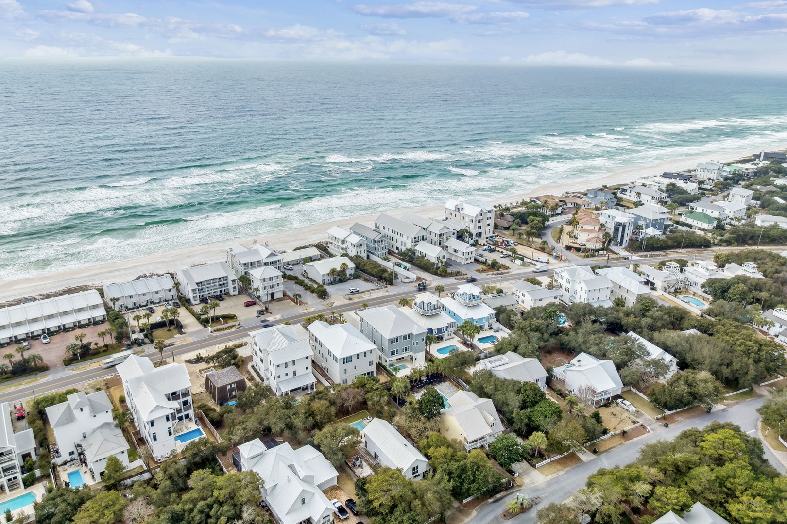 Stunning aerial view of beachfront vacation homes nestled between pristine white sand and lush coastal vegetation.