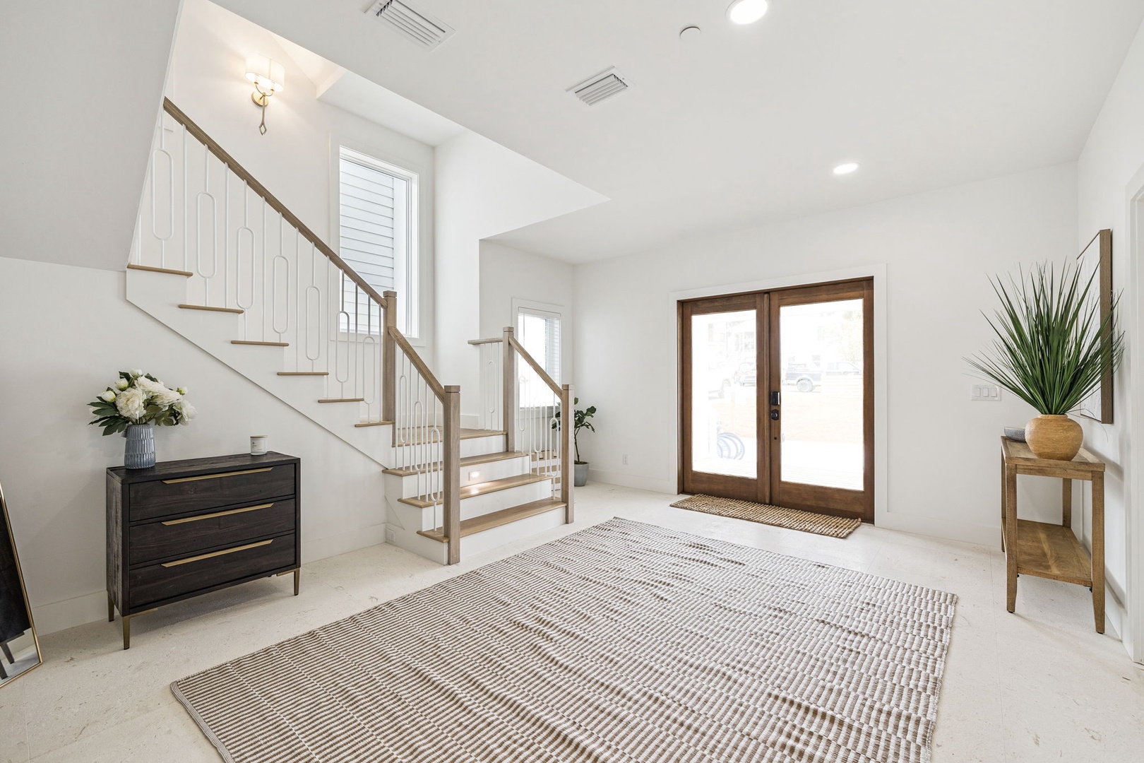 Step into your welcoming entryway, where natural light floods through French doors and a striking staircase leads to your private retreat above.