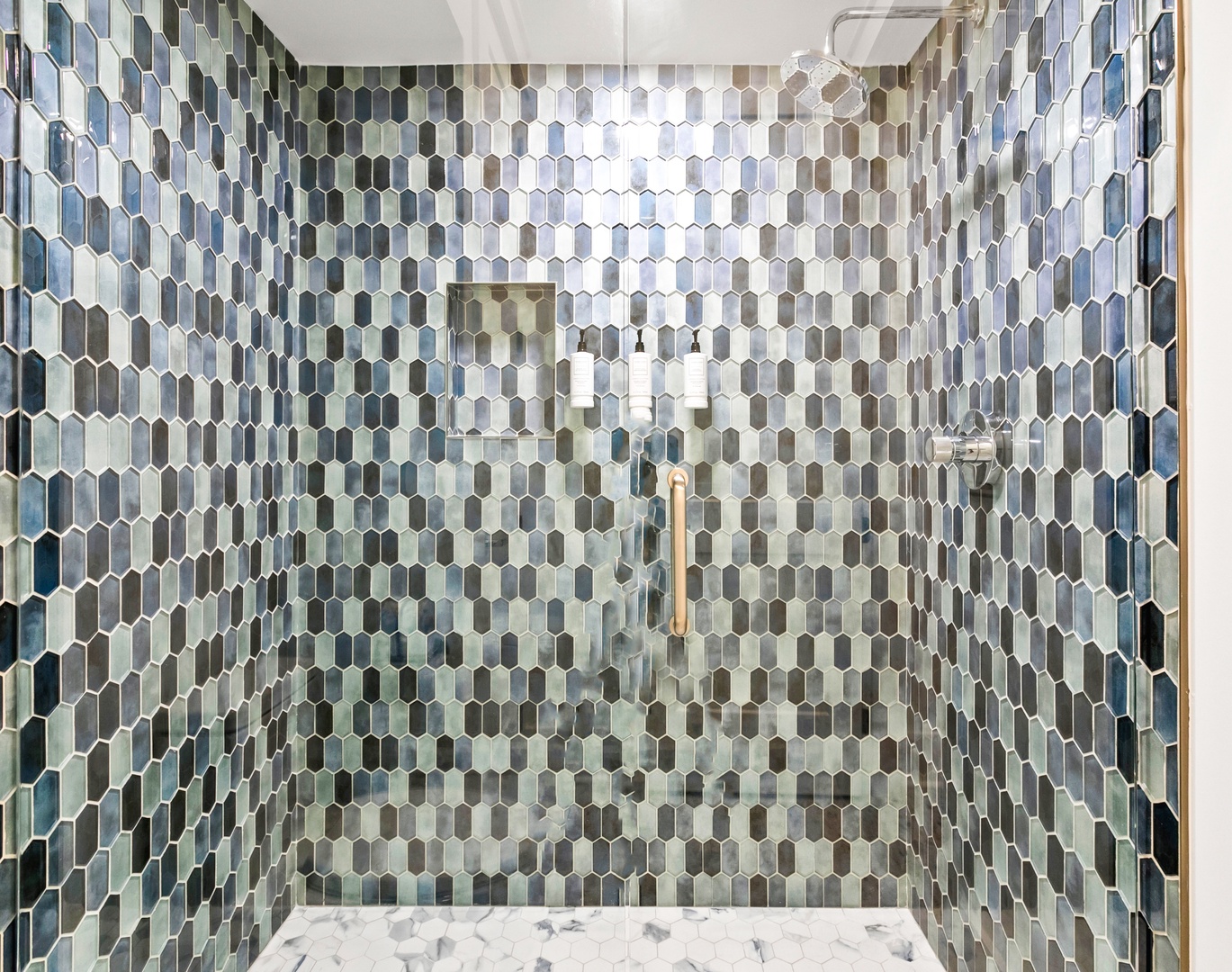 Step into your beautifully tiled glass-enclosed shower, featuring stunning hexagonal mosaic walls in soothing ocean hues and elegant marble flooring beneath your feet.