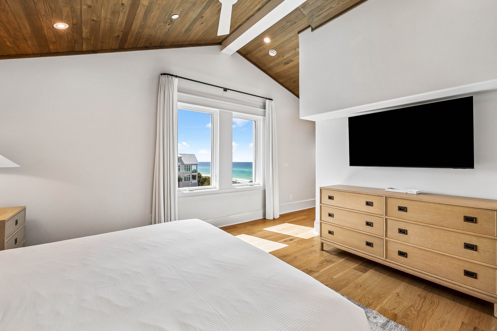 Wake up to stunning ocean views framed by natural light in your serene bedroom retreat, where elegant wood-toned furnishings and vaulted ceilings create a peaceful coastal escape.