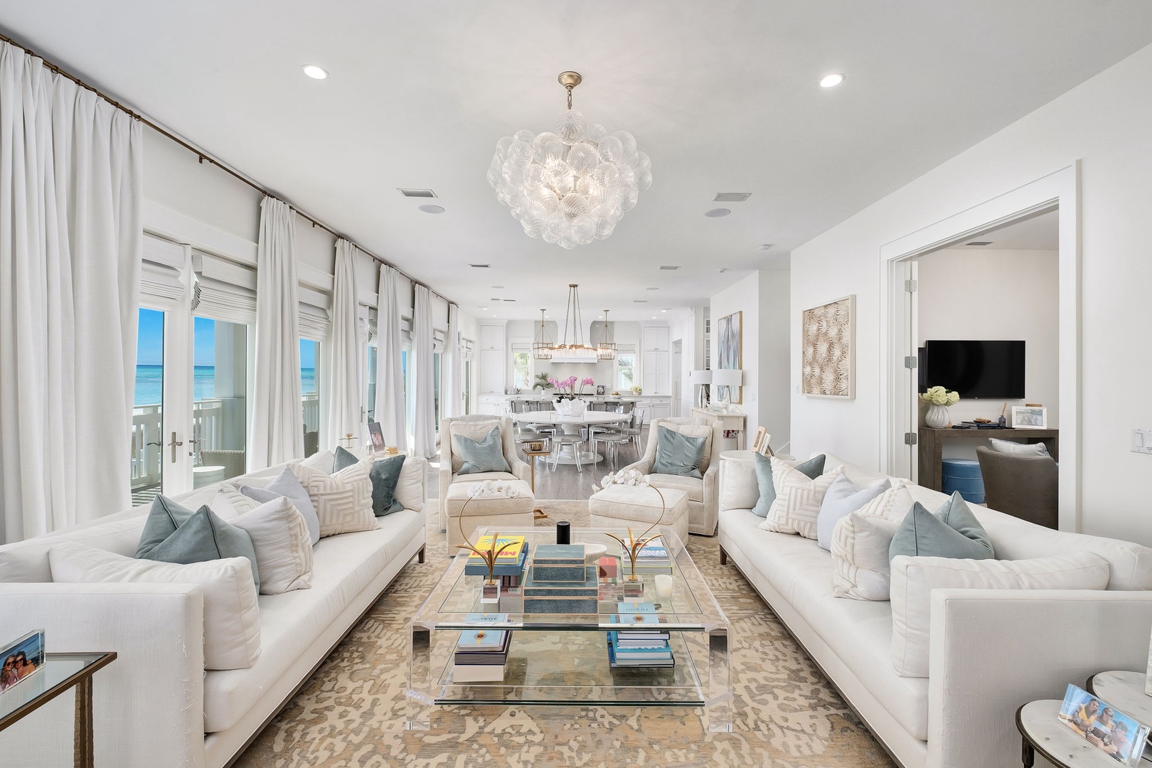Relax in your elegant living space filled with natural light and stunning sea views. Plush sofas, a sparkling chandelier, and coastal decor create a serene escape.
