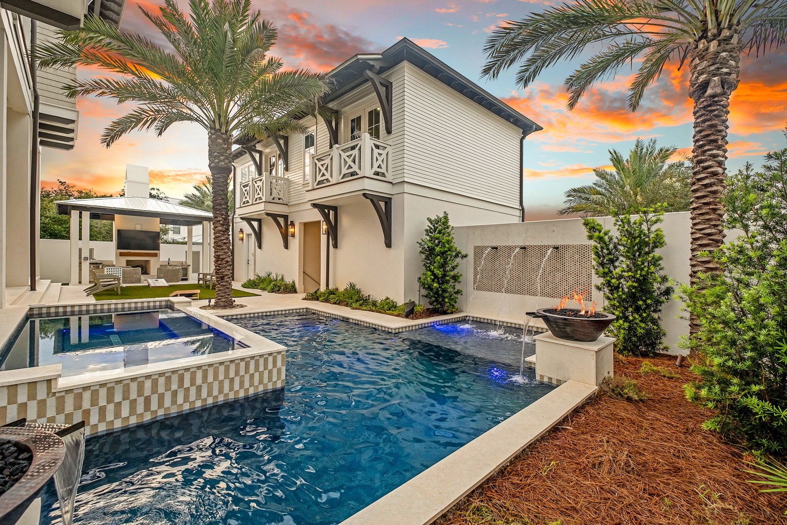 Stunning vacation home framed by swaying palms and a vibrant sunset, featuring a beautifully designed pool with integrated spa and water features for your ultimate retreat.