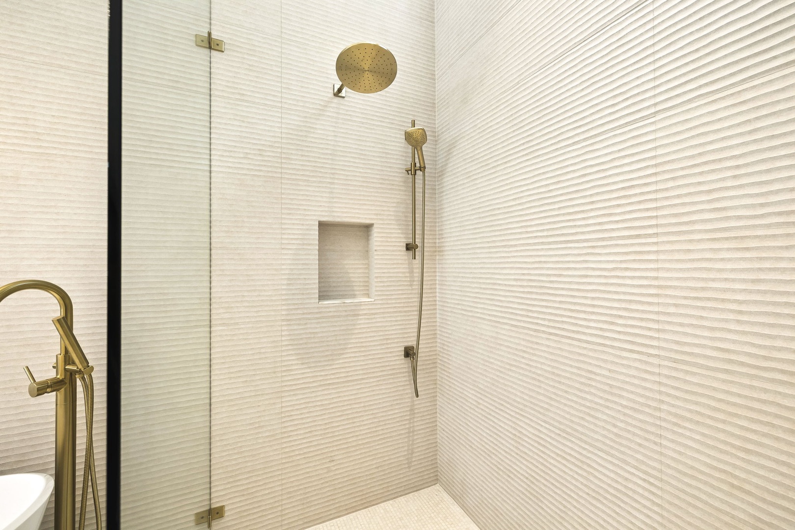 Step into your private spa-like retreat with elegant textured tile, rainfall and handheld showers, and chic gold fixtures that turn every rinse into a refreshing escape.