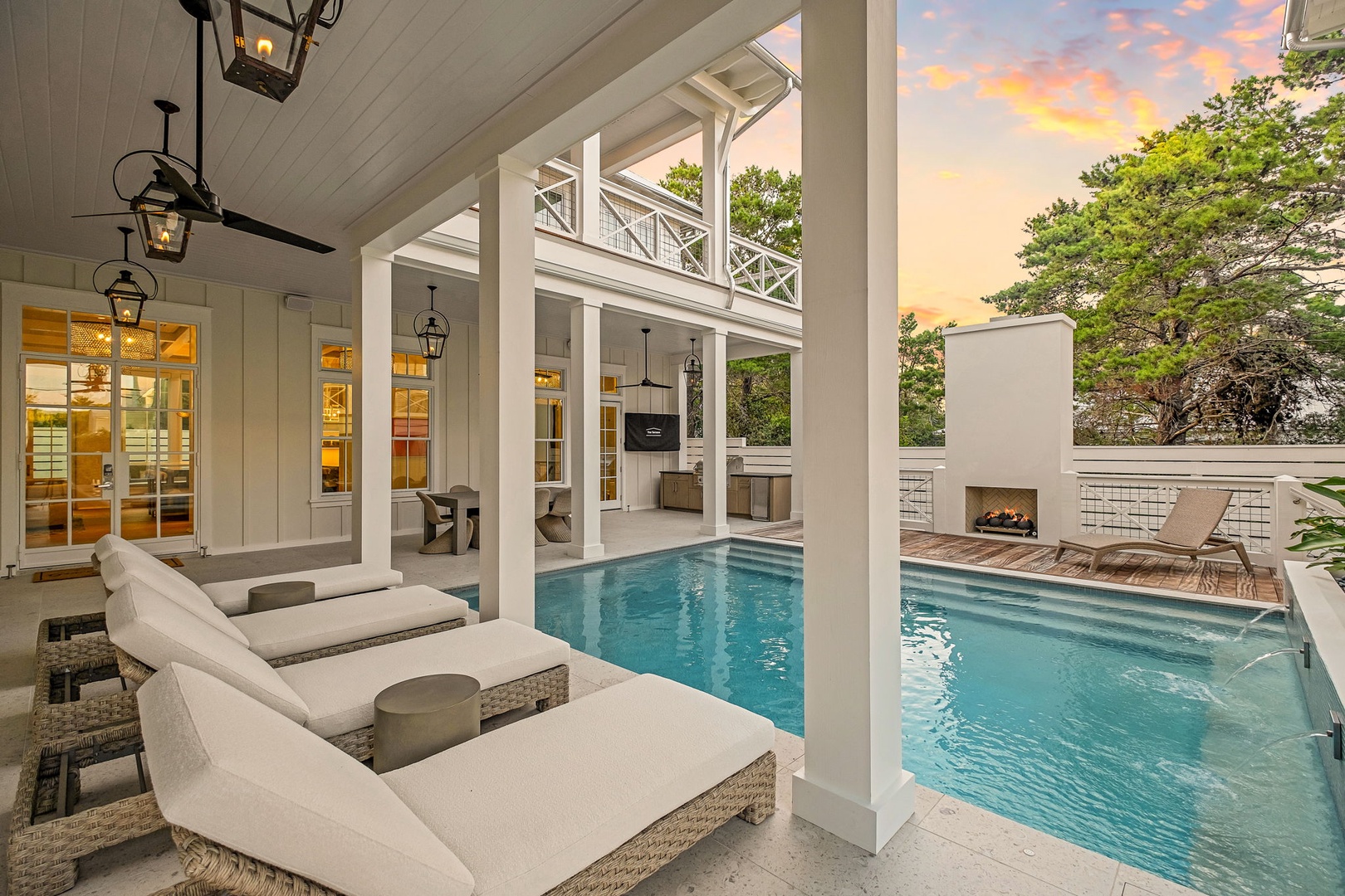 A covered outdoor space frames your private pool and elegant fireplace lounge, wrapped in sunset hues and lush greenery—your perfect retreat awaits.