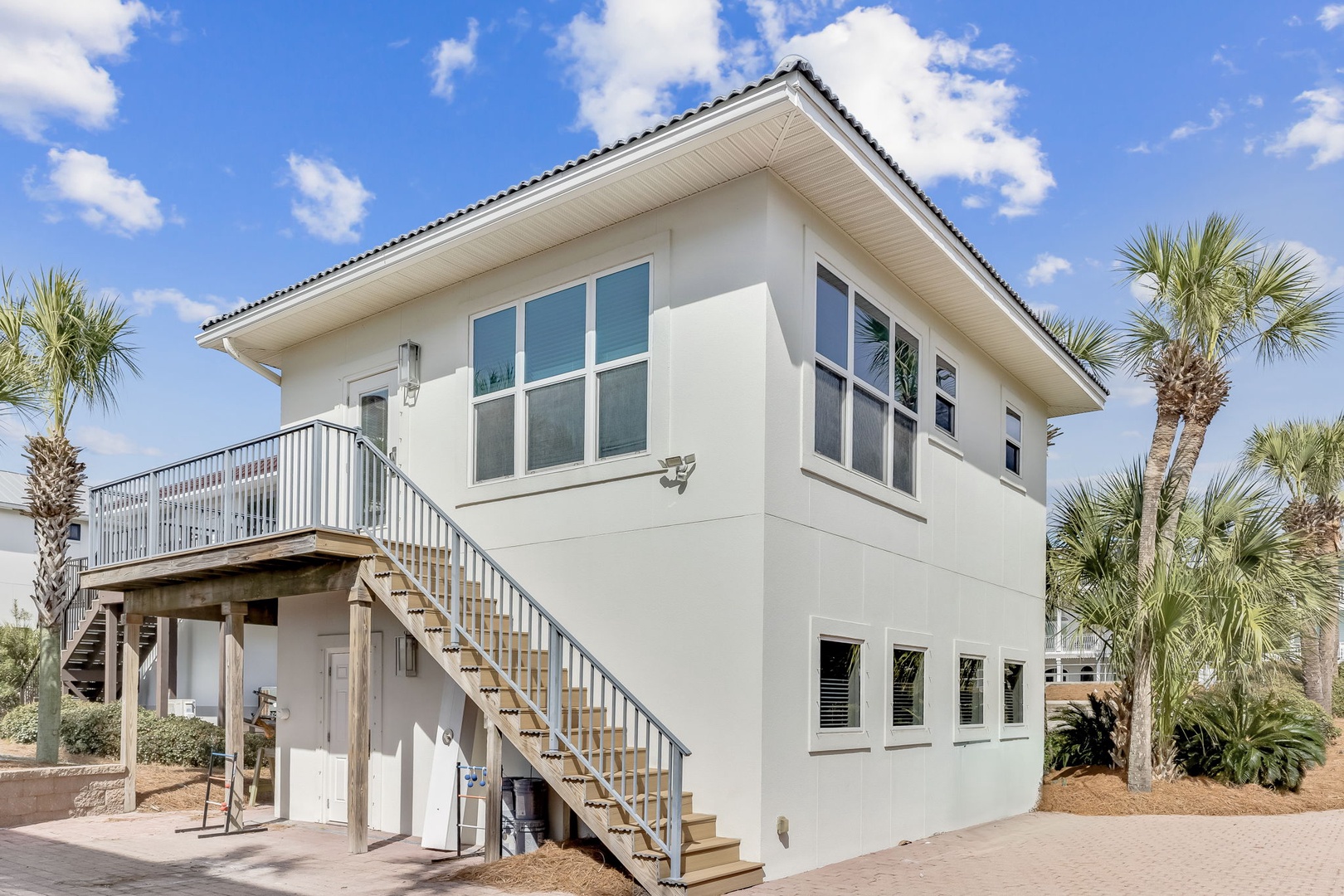 Modern two-story coastal home with palm trees and outdoor stairs, offering a tropical retreat experience.