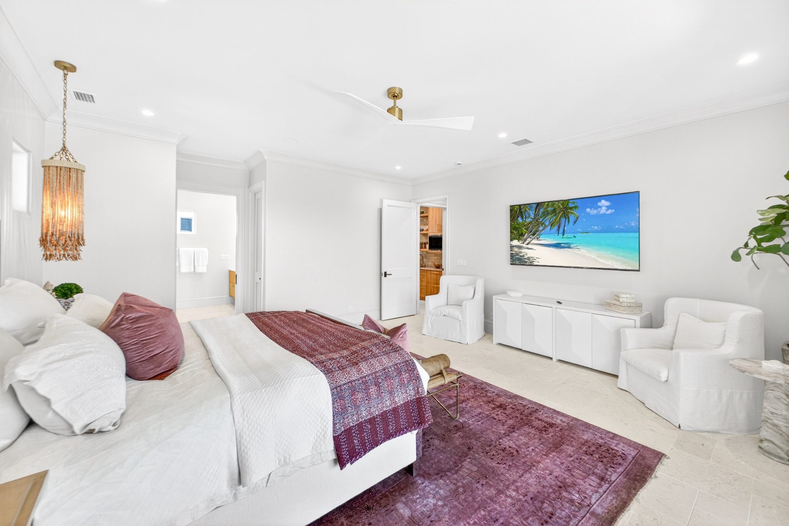 Your spacious bedroom sanctuary features a plush bed, cozy seating area, and a mounted TV for relaxing evenings. Bright, airy design and tropical artwork add a calming touch.