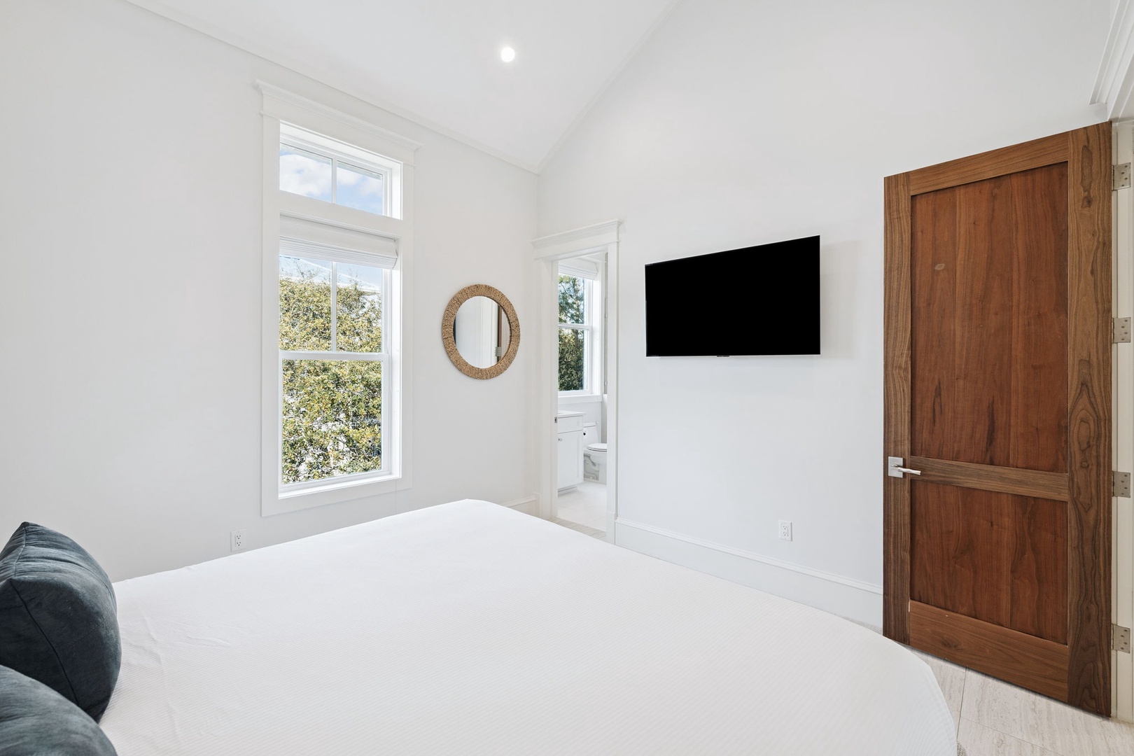 Sink into crisp white linens in your peaceful bedroom, complete with modern TV and charming garden views through bright windows.