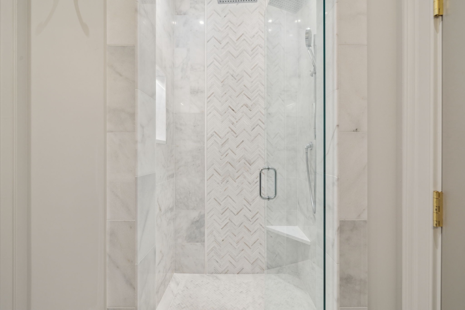 Step into your luxurious marble-tiled shower, where elegant herringbone accents and a rainfall showerhead await your morning refresh.