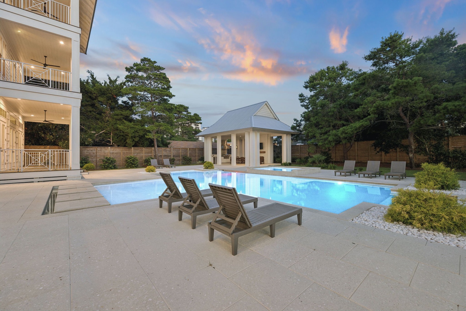 A sparkling pool surrounded by mature pines and loungers awaits under soft twilight skies, offering a peaceful retreat at the heart of the property grounds.