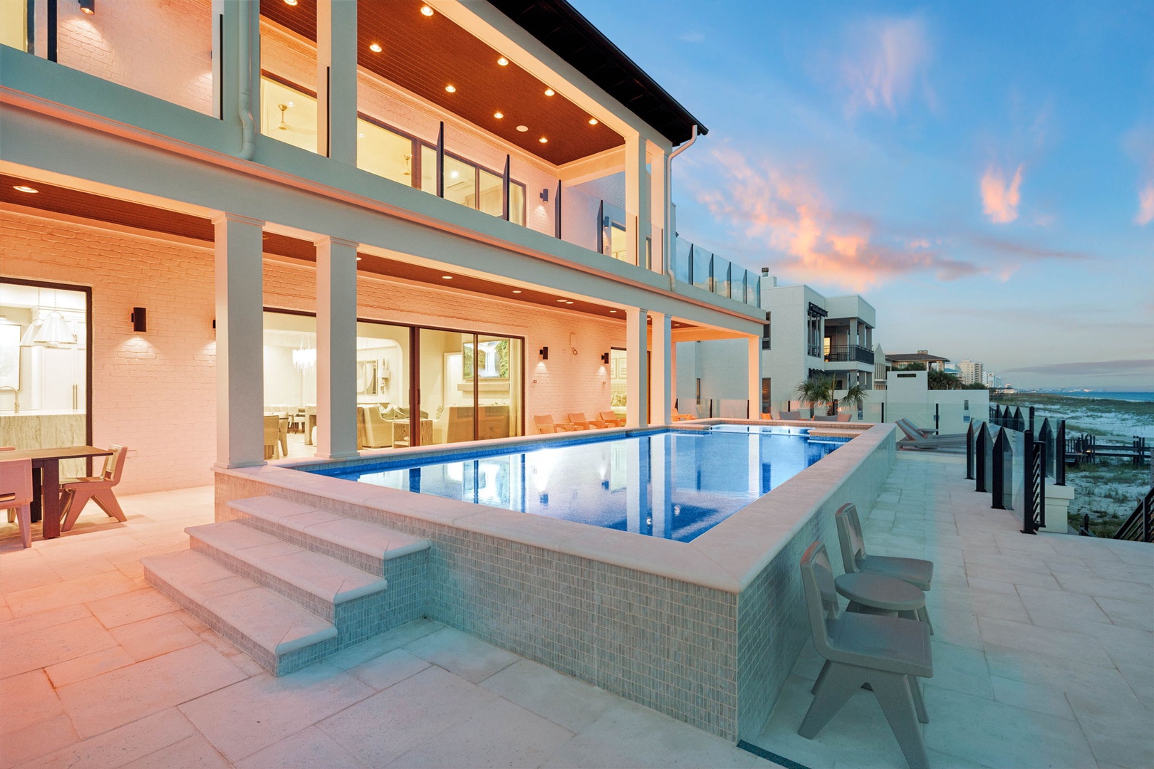 Modern beachfront architecture featuring an elevated infinity pool, spacious terrace, and stunning coastal views at twilight.
