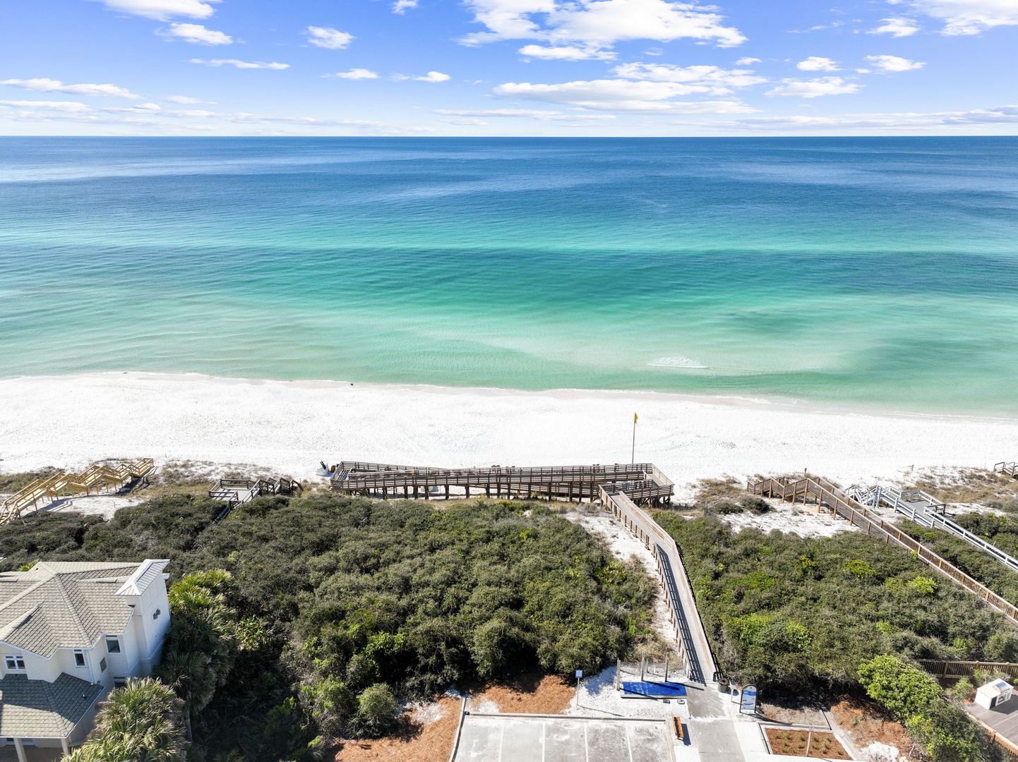 Stunning aerial view showcases pristine emerald waters and sugar-white sand beach with convenient boardwalk access to the shoreline.