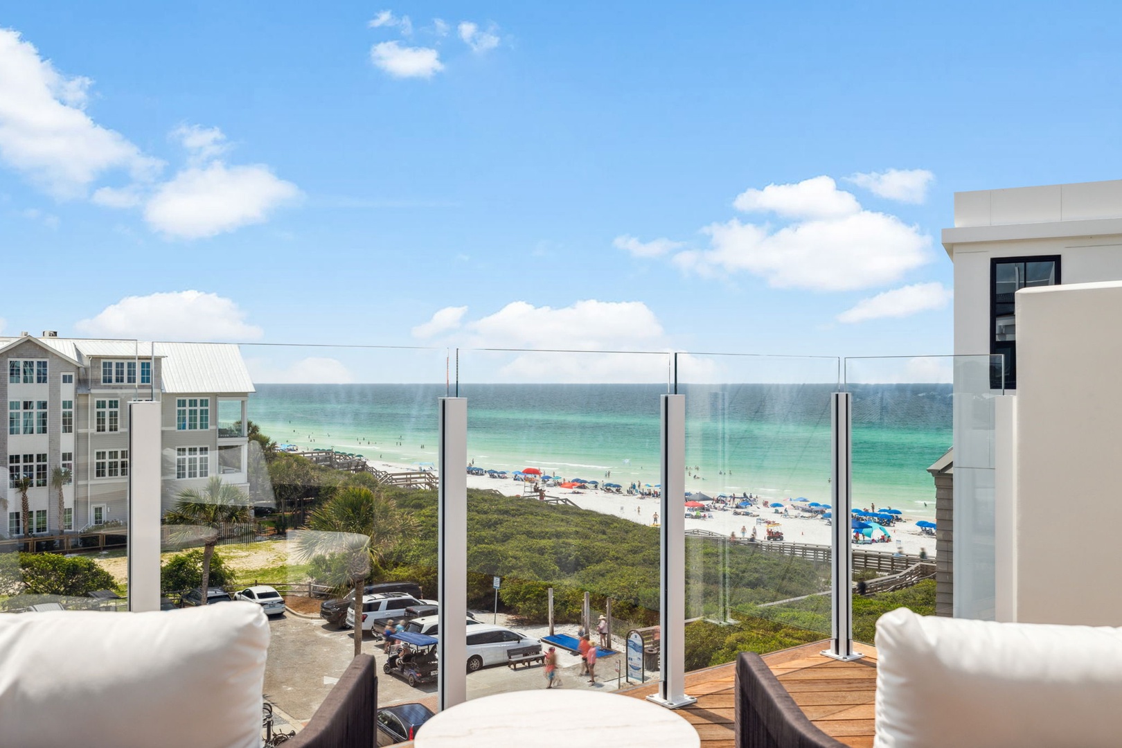 Stunning beachfront views showcase pristine white sand and turquoise waters, framed by a glass-railed balcony. Relax on comfortable outdoor seating while soaking in the coastal paradise.