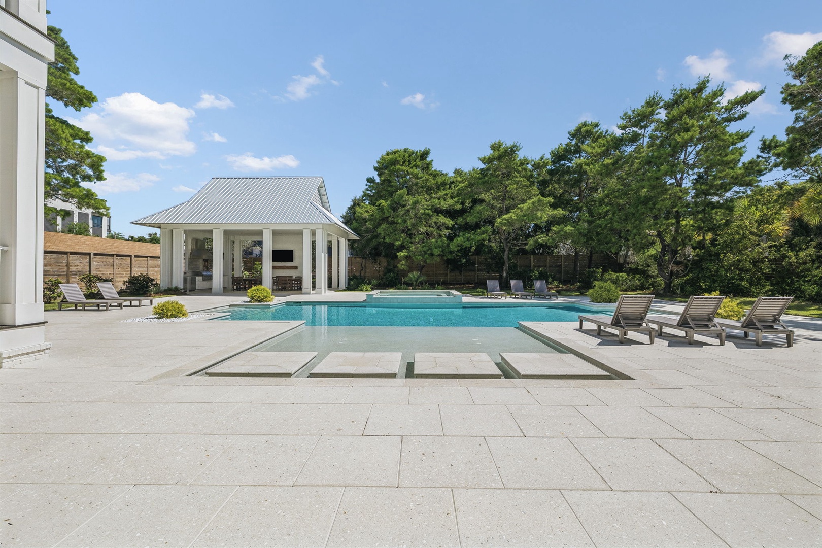 A stunning poolside retreat featuring a classic covered pavilion, expansive sundeck, and lush tree-lined backdrop—perfect for outdoor relaxation and summer gatherings.