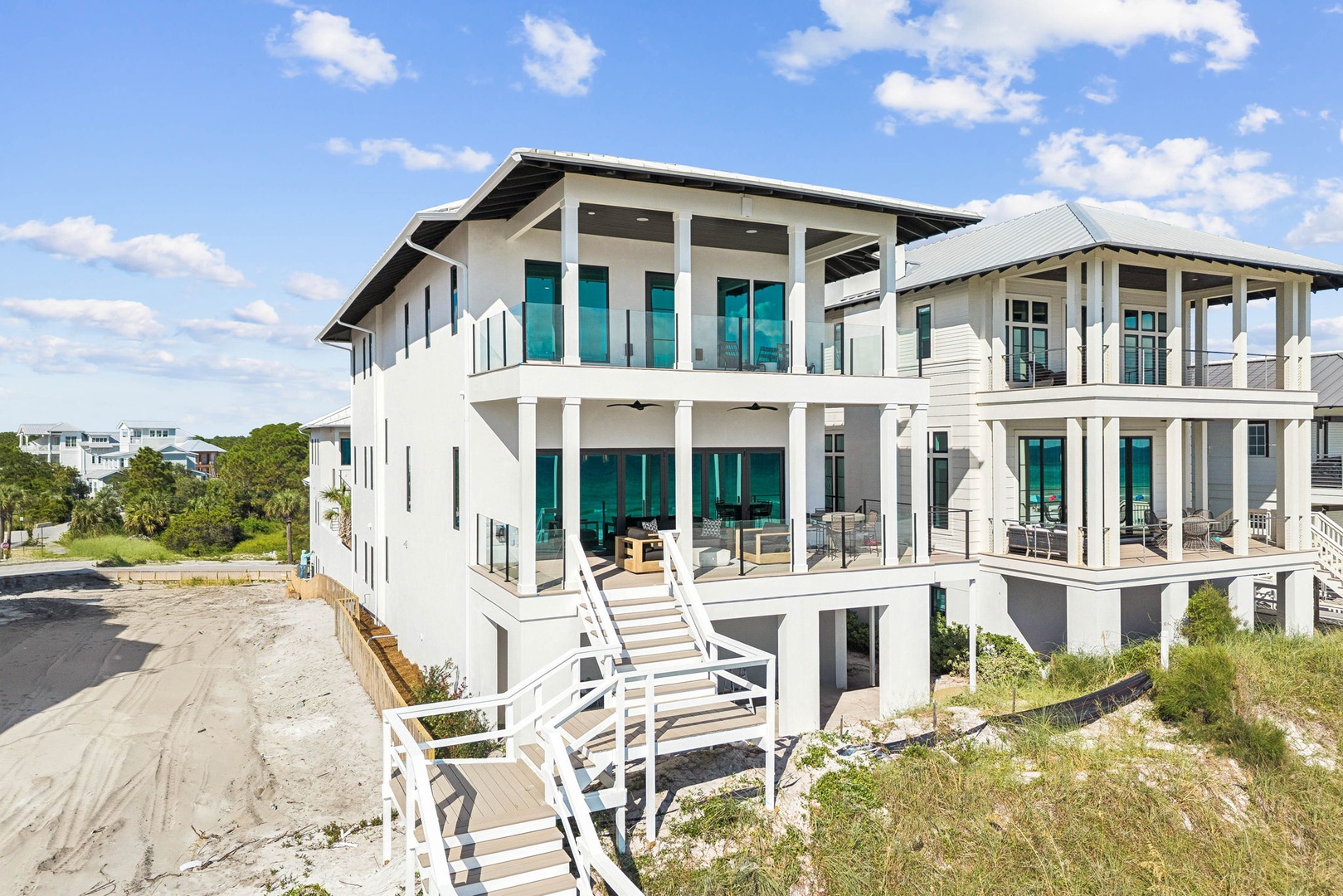 A striking modern coastal property features expansive balconies and generous windows positioned to capture ocean breezes, set within a natural dune landscape near the beach.
