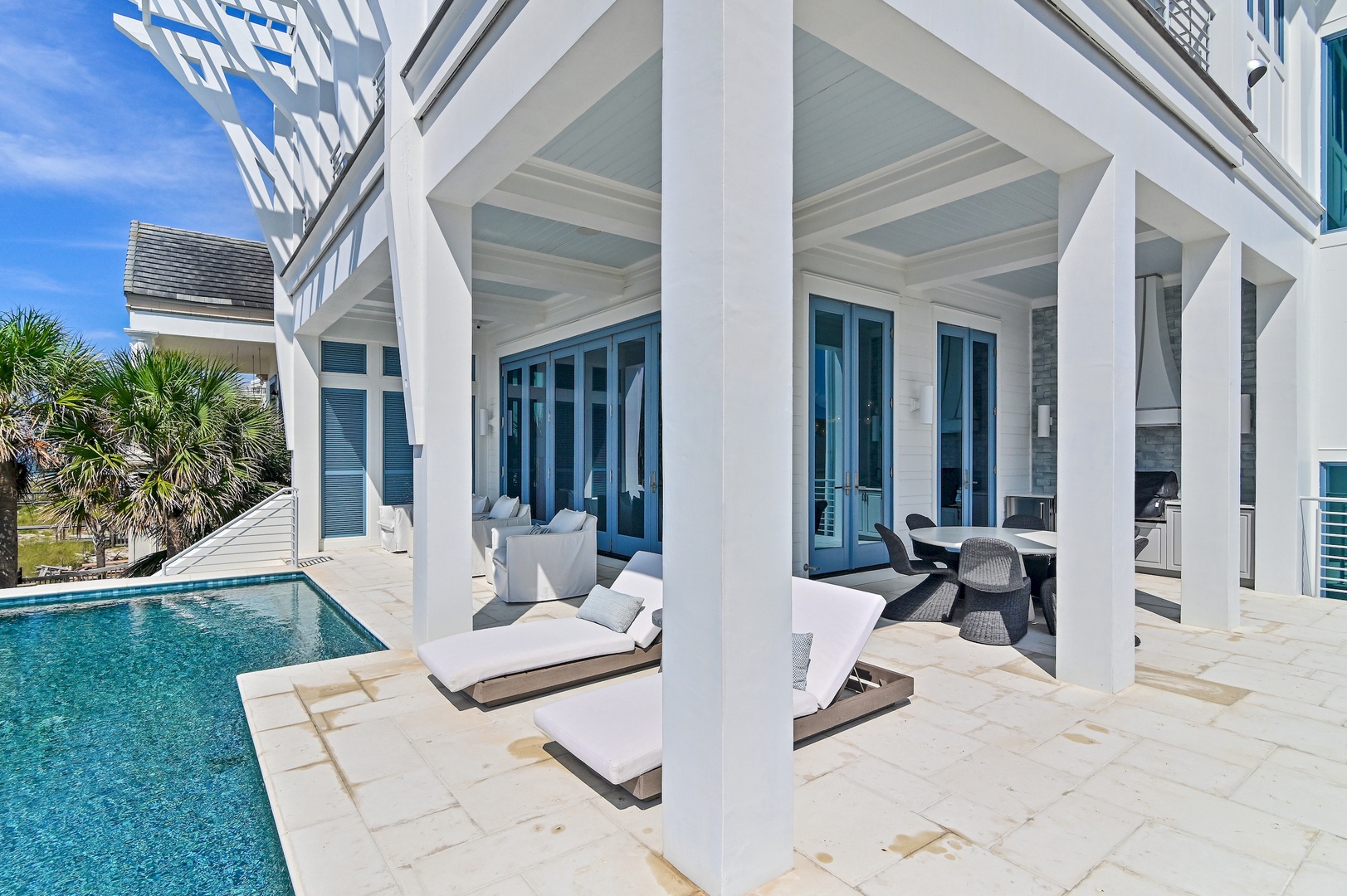 Relax poolside under your covered patio, where cushioned loungers and dining space frame stunning blue French doors. Your private oasis awaits beneath a crisp white-beamed ceiling.