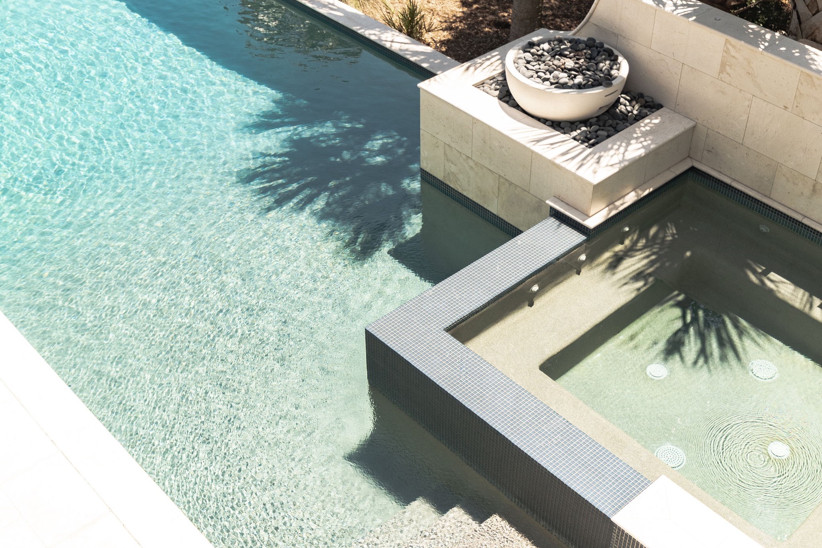 Aerial view showcasing the property's multi-level pool design with contemporary stone features and decorative water elements, framed by landscaped outdoor areas.
