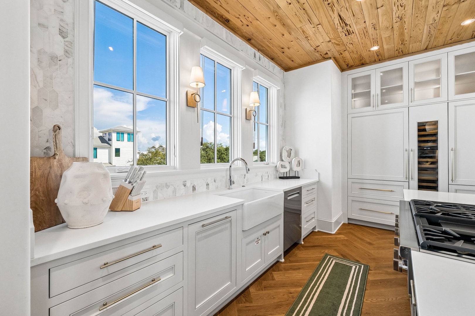Step into your gourmet kitchen with a stunning wood plank ceiling, farmhouse sink, and sunlit windows framing views of the coastal neighborhood—your home away from home.