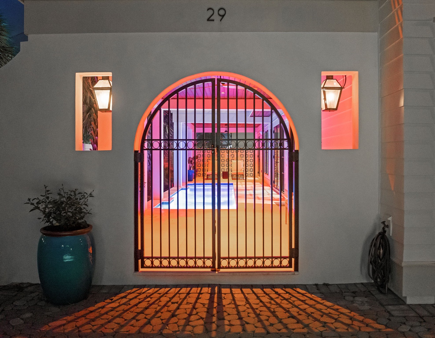 Charming entrance to property #29 features elegant arched gateway with decorative ironwork, flanked by warm lantern lighting and tropical plantings.